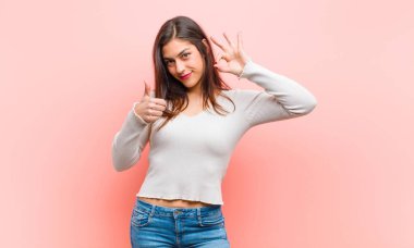 Genç, güzel bir kadın kendini mutlu, şaşkın, tatmin olmuş ve şaşırmış hissediyor. İyi olduğunu gösteriyor ve işaret ediyor. Pembe arka plana gülümsüyor..