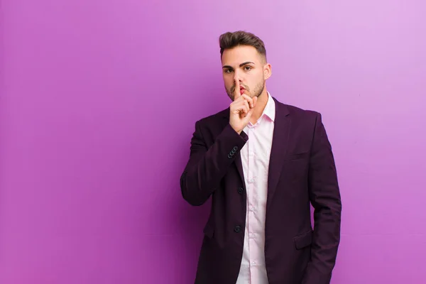 young hispanic man asking for silence and quiet, gesturing with finger in front of mouth, saying shh or keeping a secret