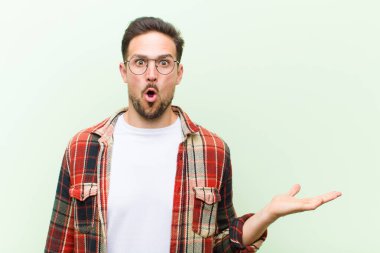 Genç yakışıklı adam şaşırmış ve şoka uğramış görünüyor, çenesi düşmüş, eli açık bir nesneyi tutuyor.