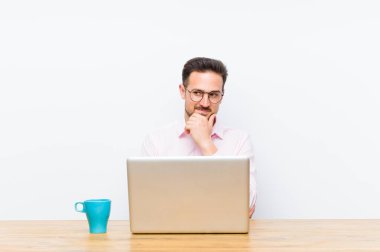 Genç yakışıklı iş adamı mutlu, kendinden emin bir ifadeyle gülümsüyor, elleri çenesinde, merak ediyor ve yan tarafa bakıyor.