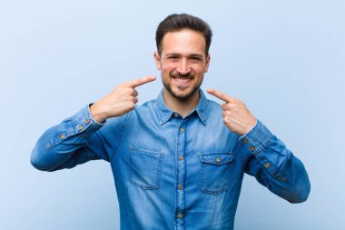 Genç yakışıklı adam, kendine güvenerek gülümsüyor. Geniş bir gülümseme, pozitif, rahat, tatmin olmuş bir tavır.
