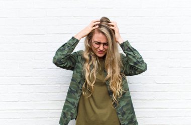 Genç sarışın kadın stresli ve hayal kırıklığına uğramış hissediyor, el ele tutuşuyor, yorgun, mutsuz ve migreni tuğla duvarın arkasında.