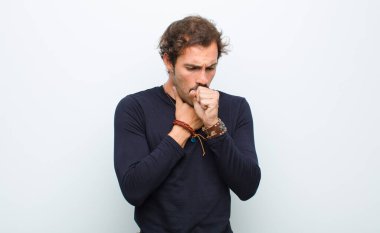 Gırtlağı ağrıyan ve grip belirtileri gösteren, ağzı beyaz duvara dayalı genç ve yakışıklı bir adam.