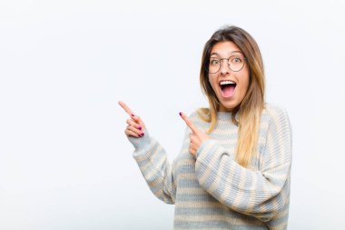 Genç, güzel bir kadın sevinçli ve şaşırmış hissediyor, şok olmuş bir ifadeyle gülümsüyor ve beyaz arka plana karşı bir tarafı işaret ediyor.