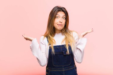 Genç, güzel bir kadın şaşkın ve şaşkın, şüpheci, farklı seçenekleri tartıyor ya da beyaz arka plana karşı komik bir ifadeyle seçiyor.