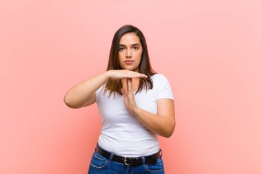Genç, güzel İspanyol bir kadın ciddi, sert, hoşnutsuz ve kızgın görünüyor. Pembe duvara karşı el hareketini durduruyor.