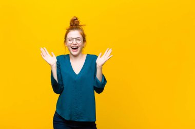 Genç kızıl saçlı kadın mutlu, heyecanlı, şaşırmış ya da şok olmuş hissediyor. Turuncu duvara karşı inanılmaz bir şeye gülümsüyor ve hayrete düşüyor.