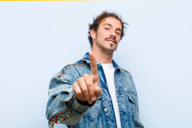 Genç yakışıklı adam gururla gülümsüyor ve gururla bir numaralı pozunu veriyor. Düz duvara karşı kendini izole edilmiş bir lider gibi hissediyor.