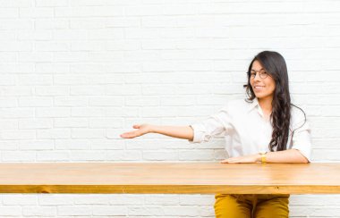 Genç, güzel, Latin bir kadın kendini mutlu ve neşeli hissediyor, gülümsüyor ve seni karşılıyor, seni bir masanın önünde dostça bir jestle içeri davet ediyor.