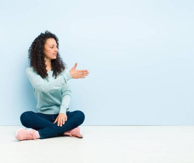 Genç, güzel bir kadın gülümsüyor, seni selamlıyor ve başarılı bir anlaşma için el sıkışmayı teklif ediyor.