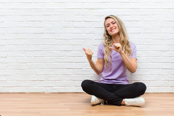 Genç sarışın güzel kadın neşeli bir şekilde gülümsüyor ve yan taraftaki fotokopi alanını gösteriyor, mutlu ve tatmin olmuş hissediyor.
