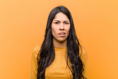 Genç, güzel İspanyol kadın şaşkın ve şaşkın hissediyor, aptal, şaşkın bir yüz ifadesiyle kahverengi duvara karşı beklenmedik bir şeye bakıyor.