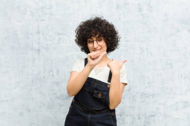 Genç, güzel afro kadın neşeyle gülümsüyor ve yan taraftaki fotokopi alanını gösteriyor, mutlu ve tatmin olmuş hissediyor.