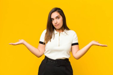 Genç güzel kadın şaşkın ve kafası karışmış hissediyor, doğru cevap veya karardan emin değil, turuncu duvara karşı izole edilmiş bir seçim yapmaya çalışıyor.