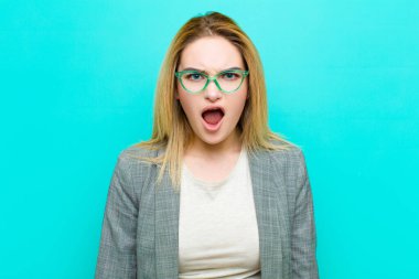 Genç, güzel, sarışın kadın dehşete kapılmış ve şok olmuş hissediyor, ağzı ardına kadar açık, düz duvara karşı şaşkınlık içinde.