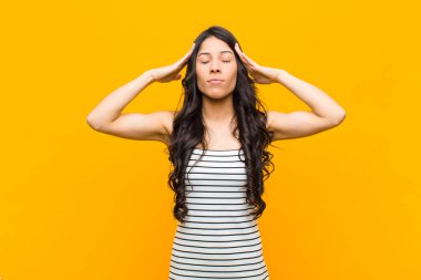 Genç ve güzel Latin kadın konsantre, düşünceli ve ilham verici görünüyor, beyin fırtınası yapıyor ve elleri turuncu duvarda hayal ediyor.