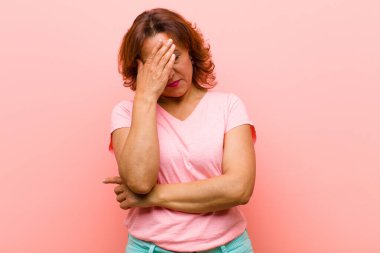 Orta yaşlı kadın stresli, utanmış ya da üzgün görünüyor, baş ağrısı var, yüzünü pembe duvara dayamış.