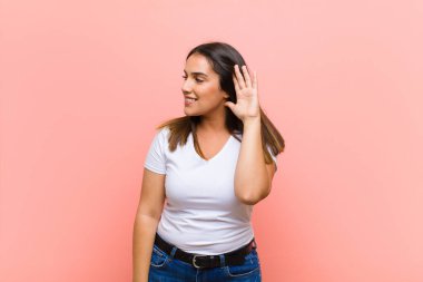 Genç ve güzel İspanyol kadın gülümsüyor ve mutlu, sevimli, romantik ve aşık, iki elini de pembe duvara dayayıp kalp şekli veriyor.