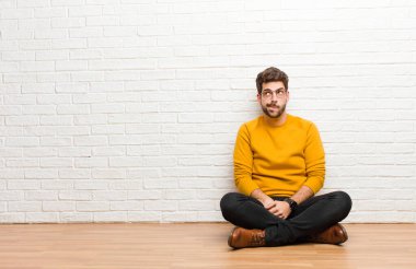Genç yakışıklı adam tuğla duvar dokusuna karşı evde oturuyor.