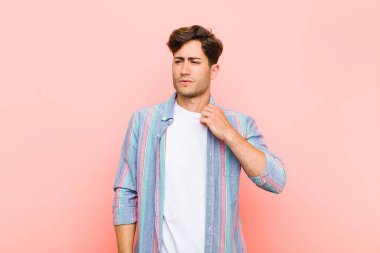Genç ve yakışıklı bir adam stresli, endişeli, yorgun ve hayal kırıklığına uğramış, gömleğini çekmiş, pembe arka plandaki problemden bıkmış görünüyor.