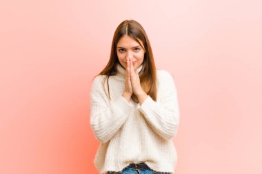 Genç, güzel bir kadın endişeli, umutlu ve dindar, avuçlarını sıkarak dua ediyor, pembe arka plana karşı af diliyor.