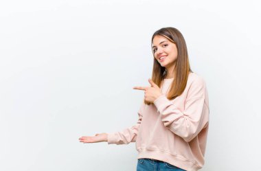 Genç, güzel bir kadın gülümsüyor, mutlu, kaygısız ve tatmin olmuş hissediyor. Fotokopi alanının beyaz arka plandaki konseptine ya da fikrine işaret ediyor.