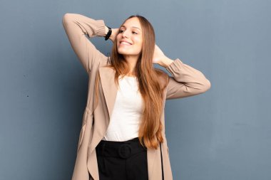 Genç ve güzel bir kadın gülümsüyor ve rahatlıyor, tatmin oluyor ve kaygısız, olumlu gülüyor ve gri arka plana karşı ürperiyor.