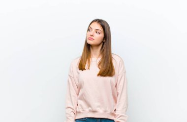 Endişeli, kafası karışık, cahil bir ifadeyle genç, güzel bir kadın, kopyalama alanına bakıyor, beyaz arkaplana karşı şüpheyle bakıyor.