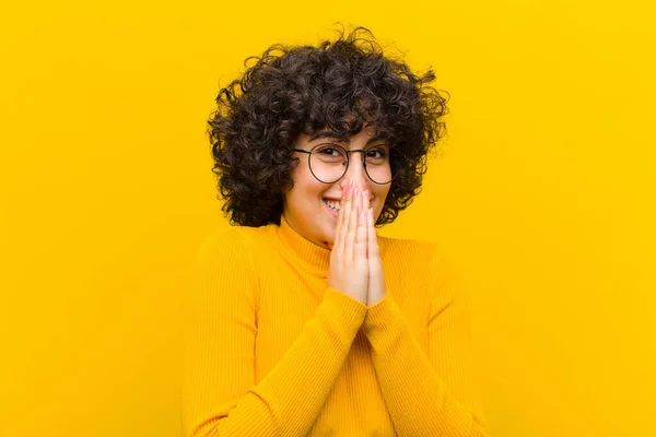 young pretty afro woman happy and excited, surprised and amazed covering mouth with hands, giggling with a cute expression