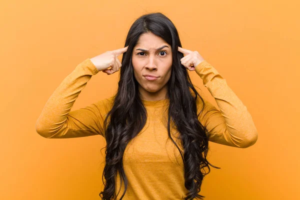 young pretty hispanic woman with a serious and concentrated look, brainstorming and thinking about a challenging problem against brown wall