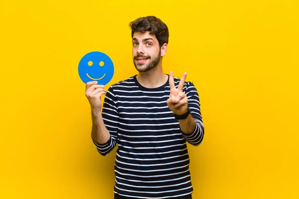 Jovem homem bonito segurando um rosto sorridente contra backgro laranja — Fotografia de Stock