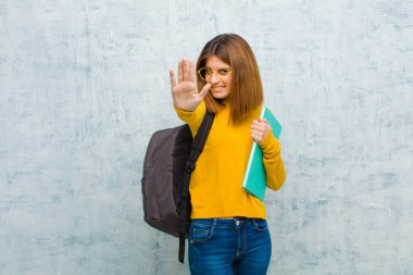 Genç bayan ciddi, mutsuz, sinirli ve hoşnutsuz görünüyor. Ya da her iki avuç içi açık şekilde, arka plandaki grunge duvarına yaslanarak dur diyor.