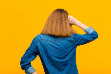 Genç, güzel bir kadın düşünüyor ya da şüphe ediyor, kafasını kaşıyor, şaşkın ve şaşkın hissediyor, sarı arka planda ya da arka planda