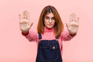 Genç ve güzel bir kadın ciddi, mutsuz, kızgın ve hoşnutsuz görünüyor. Ya da pembe arka planda her iki avucunuzu açarak durmanızı söylüyor.