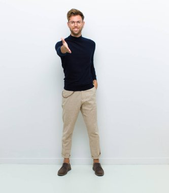 Genç adam gülümsüyor, mutlu, kendinden emin ve arkadaş canlısı görünüyor. Anlaşmayı bağlamak için el sıkışma teklif ediyor. Beyaz arka plana karşı işbirliği yapıyor.