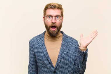 Genç sarışın işadamı şaşırmış ve şoka uğramış görünüyor, çenesi düşmüş, bir objeyi elinde açık bir elle tutuyor.