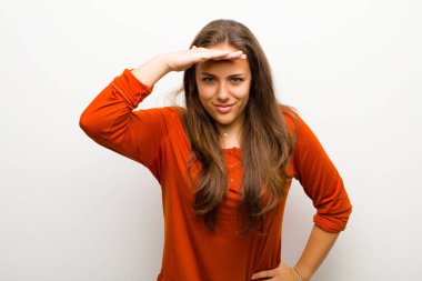 Genç kadın şaşkınlık ve şaşkınlık içinde bakıyor, uzaktan bakıyor, beyaz arka planı izliyor ya da araştırıyor.