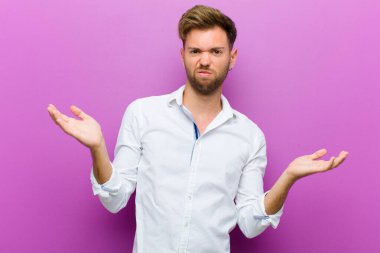 Genç adam şaşkın, şaşkın ve stresli görünüyor, farklı seçenekler arasında merak ediyor, mor arka planda belirsizlik hissediyor