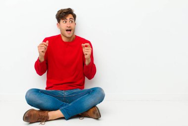 Genç yakışıklı adam çok mutlu ve şaşırmış görünüyor, başarıyı kutluyor, bağırıyor ve yerde zıplıyor.