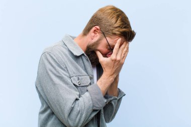 Genç, sarışın, yetişkin bir adam üzgün, hayal kırıklığına uğramış bir bakışla gözlerini kapatıyor, ağlıyor, yan gözle bakıyor.