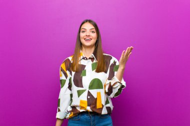 Genç, güzel bir kadın kendini mutlu, şaşırmış ve neşeli hissediyor. Olumlu bir tavırla gülümsüyor. Mor arka plana karşı bir çözüm ya da fikir buluyor.