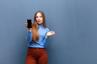 young pretty woman using a smart phone against blue wall with a copy space
