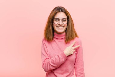 Genç, güzel bir kadın kendini mutlu, pozitif ve başarılı hissediyor. Göğsünde V şeklinde eller yapıyor. Pembe arka plana karşı zafer ya da barış gösteriyor.