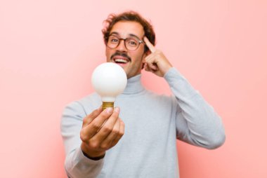 Genç yakışıklı adamın pembe düz duvara karşı ampulü olan bir fikri var.