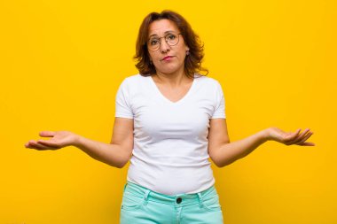 Orta yaşlı kadın şaşkın ve kafası karışık, doğru cevap ya da karardan emin değil, sarı duvara karşı bir seçim yapmaya çalışıyor.