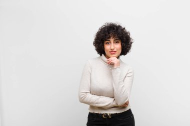 Genç, güzel bir afro kadın mutlu görünüyor ve gülümsüyor. Elleri çenesinde, merak ediyor ya da soru soruyor. Seçenekleri karşılaştırıyor.