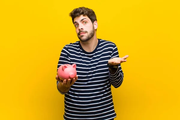 Joven hombre guapo sosteniendo una alcancía contra fondo naranja — Foto de Stock