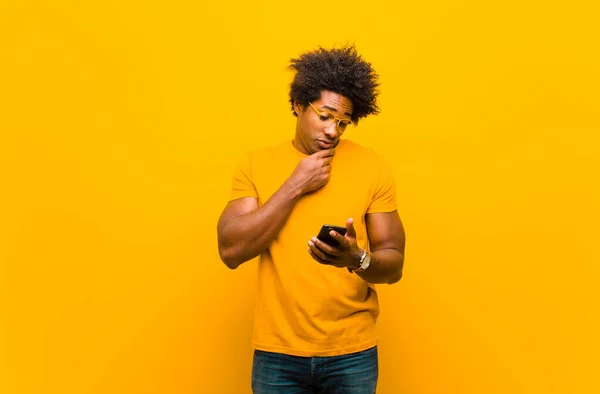 Молодий афроамериканський чоловік зі смартфоном проти апельсинового спини — стокове фото
