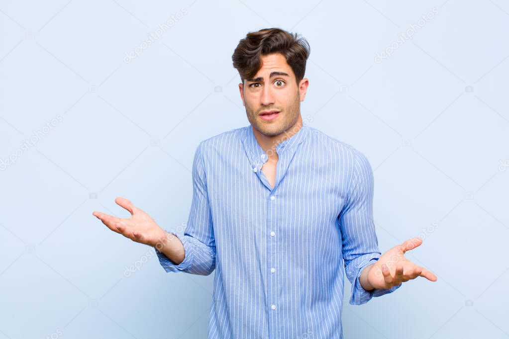 young handsome man feeling clueless and confused, not sure which choice or option to pick, wondering against blue background