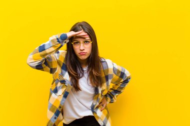 Genç, güzel bir kadın şaşkınlık ve şaşkınlık içinde bakıyor. Alnı açık, uzaklara bakıyor, turuncu duvara bakıyor ya da bakıyor.